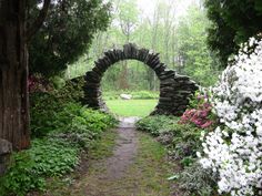 a stone arch in the middle of a lush green forest filled with flowers and trees