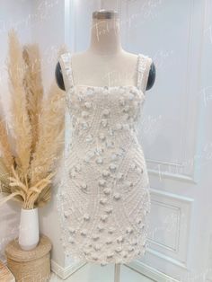 a white dress on display next to a vase with dried grass in it and a fake feather