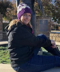 a woman sitting on the ground in front of a statue wearing a knitted hat