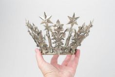 a hand holding a silver crown with stars on it