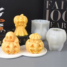 three halloween candles sitting on top of a white plate next to a book and vase