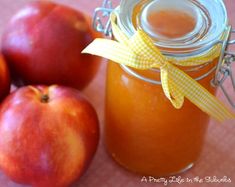 an apple jam in a glass jar next to two apples