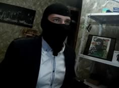 a man wearing a black mask in front of a wall with pictures on the walls