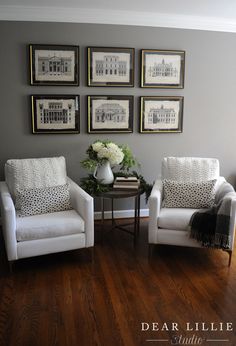 two white chairs sitting next to each other on top of a hard wood floor in front of framed pictures