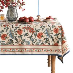 a table topped with fruit and a vase filled with red flowers next to a candle