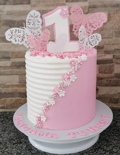 a pink and white birthday cake with butterflies on it's top is sitting on a plate