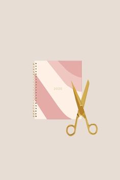 a pair of gold scissors sitting on top of a pink and white striped binder