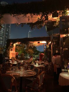 people are sitting at tables in the middle of an outdoor dining area with tall buildings behind them