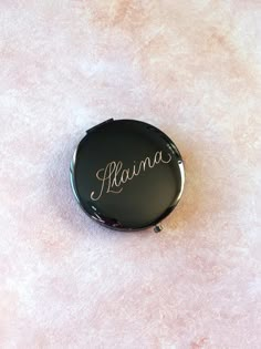 a black compact case with the word mama written on it sitting on a pink surface