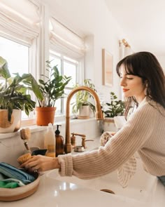 a woman washes her hands in the kitchen sink while plants are on the window sill