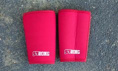 two red knee pads with the word strong written on them are laying on concrete and there is no image to describe