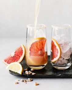 grapefruit and orange juice being poured into wine glasses on a tray with ice