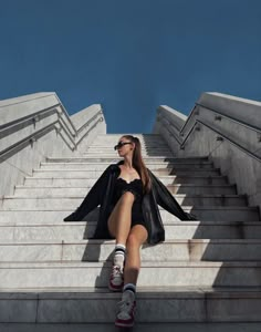 a woman is sitting on some steps with her legs crossed and wearing sunglasses, black coat and skirt