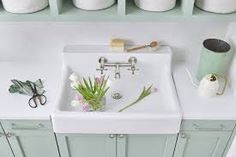 a white sink sitting in the middle of a kitchen next to green cupboards and drawers