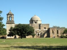 an old building with two towers and people walking in the grass near by on a sunny day