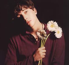 a young man holding two daisies in his hands