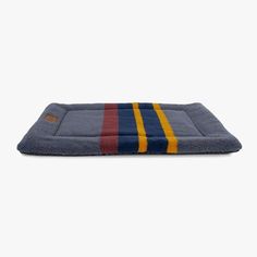 a blue dog bed with red, yellow and blue stripes on the bottom is shown in front of a white background