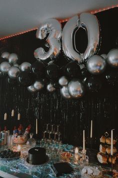 a table topped with lots of silver balloons and black plates filled with cake on top of it