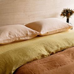 two pillows on top of a bed next to a vase filled with flowers and plants