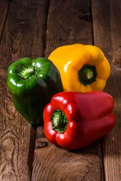 three different colored peppers sitting on top of a wooden table next to eachother