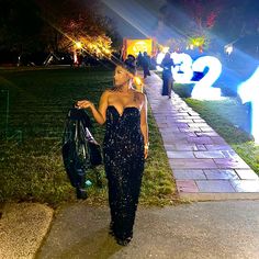 a woman in a black dress is walking down the street at night with her hand on her hip