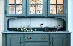 a blue china cabinet with glass doors on the top and bottom, in front of a white wall