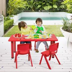 two children sitting at a red table with plates of food in front of an outdoor swimming pool