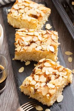 two pieces of cake with almonds on top and a glass of coffee in the background