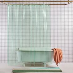 a bath tub sitting under a shower curtain next to a rug and towel on the floor