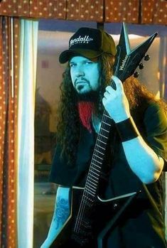 a man with long hair holding a guitar in his right hand and wearing a hat