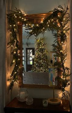 a christmas tree in the corner of a room with lights on it and a mirror behind it