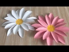 two paper flowers sitting on top of a wooden table with white and pink petals next to each other