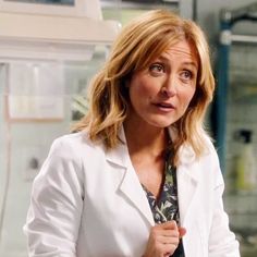 a woman in a white lab coat holding a tie up to her chest and looking off into the distance