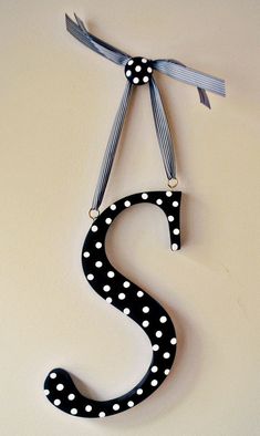 a black and white polka dot letter s hanging from a wall with ribbon on it