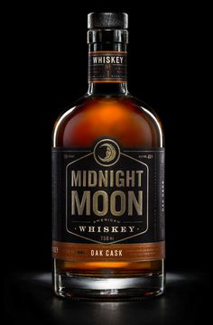 a bottle of whiskey sitting on top of a table next to a black background with the words midnight moon written across it