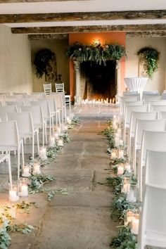 rows of white chairs are lined up with candles and greenery in front of the fireplace