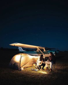 two people sitting in chairs next to a tent at night with an airplane on the background