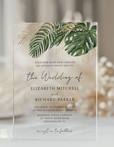 an elegant wedding card with tropical leaves and greenery is displayed on top of a table