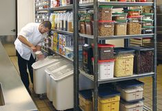 a man standing in front of a shelf filled with containers and bins full of food