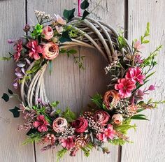 a wreath with pink flowers and greenery hanging on a wooden door, next to a candle