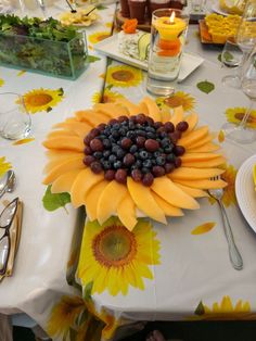 a sunflower centerpiece with grapes and blueberries sits on a table in front of other place settings