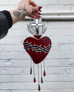 a hand holding a red heart shaped clock with chain attached to it's side