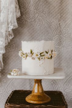 a white cake with flowers on it sitting on top of a wooden stand in front of a wall