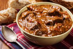 a bowl of beef stew with bread on the side