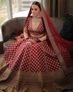 a woman sitting on top of a couch wearing a red and gold wedding dress with a veil