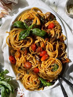 a white bowl filled with pasta and vegetables on top of a table next to utensils