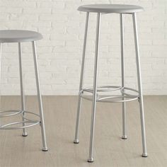 two stools sitting next to each other in front of a white brick wall and wooden floor