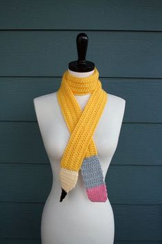 a white mannequin with a yellow scarf on it's neck and a crocheted pencil in the middle