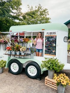 a woman standing in the doorway of a food truck with flowers on it's side