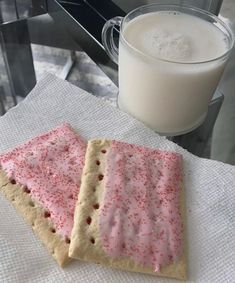 two crackers with pink and red sprinkles next to a glass of milk